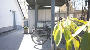 A bicycle parked under a covered area with a potted plant nearby.