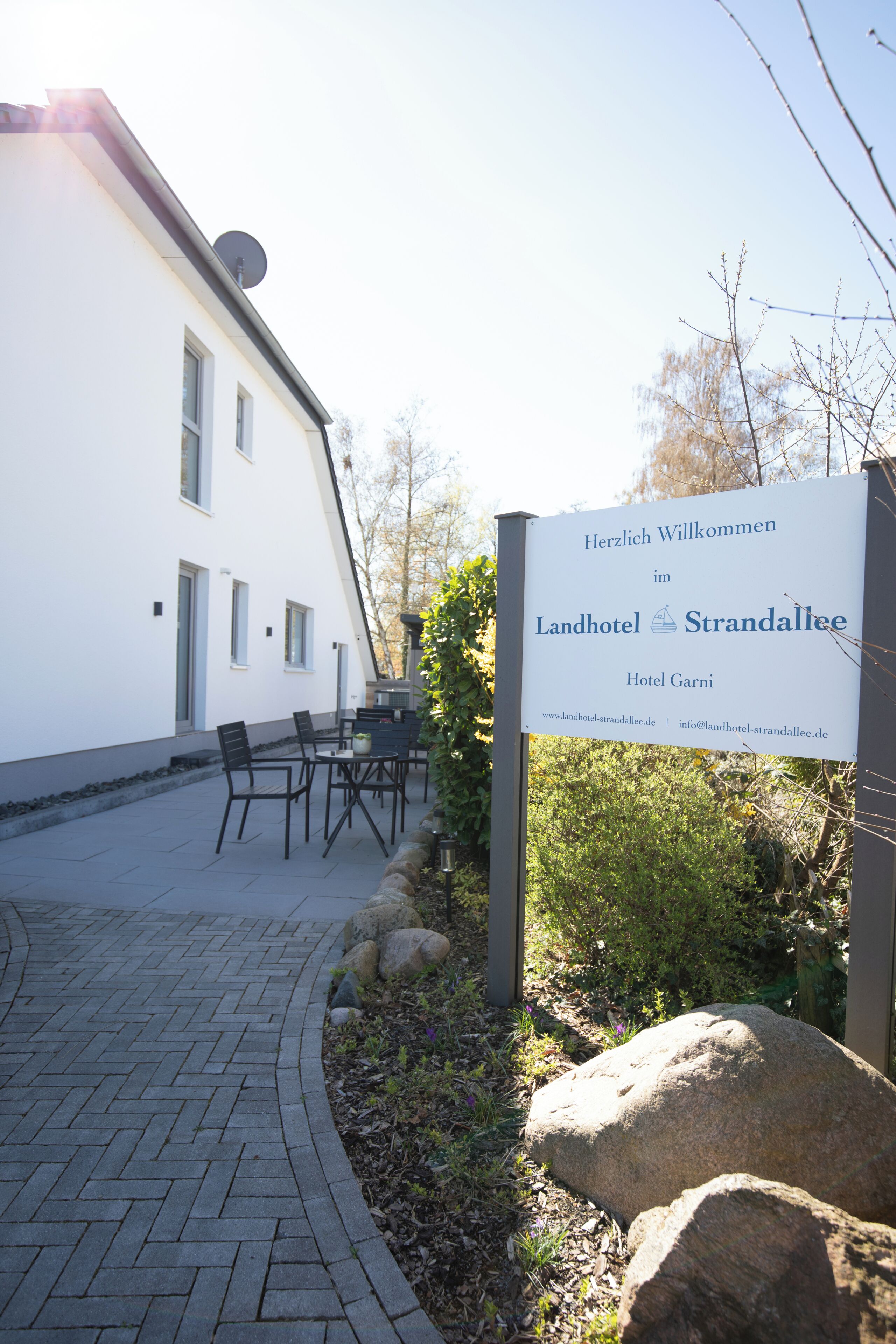 Señal de Landhotel Strandallee, Hotel Garni, con terraza al aire libre y un camino pavimentado.