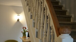 A staircase with white balusters and a wooden handrail, leading to a landing with a green chair and a small table with a vase of flowers.