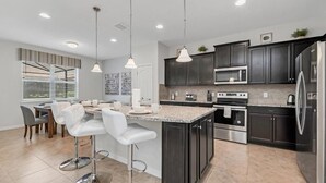 A modern kitchen with dark cabinets, stainless steel appliances, and a central island with bar stools.
