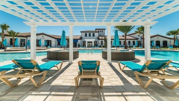 A poolside area with lounge chairs, a pergola, and a building in the background.