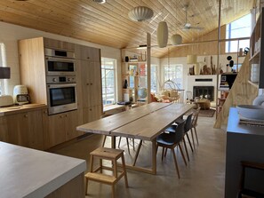 A modern kitchen with wooden cabinetry, a large dining table, and a cozy seating area. - Hoot Owl Ranch - Joshua Tree Boulder View Cabin (Yucca Valley)
