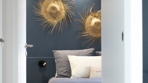 A modern bedroom with a bed, dark blue walls, and two decorative wall hangings. - Feet in the sand (La Forêt-Fouesnant)