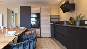 A modern kitchen with dark cabinetry, a built-in oven, and a hanging light fixture. - Feet in the sand (La Forêt-Fouesnant)