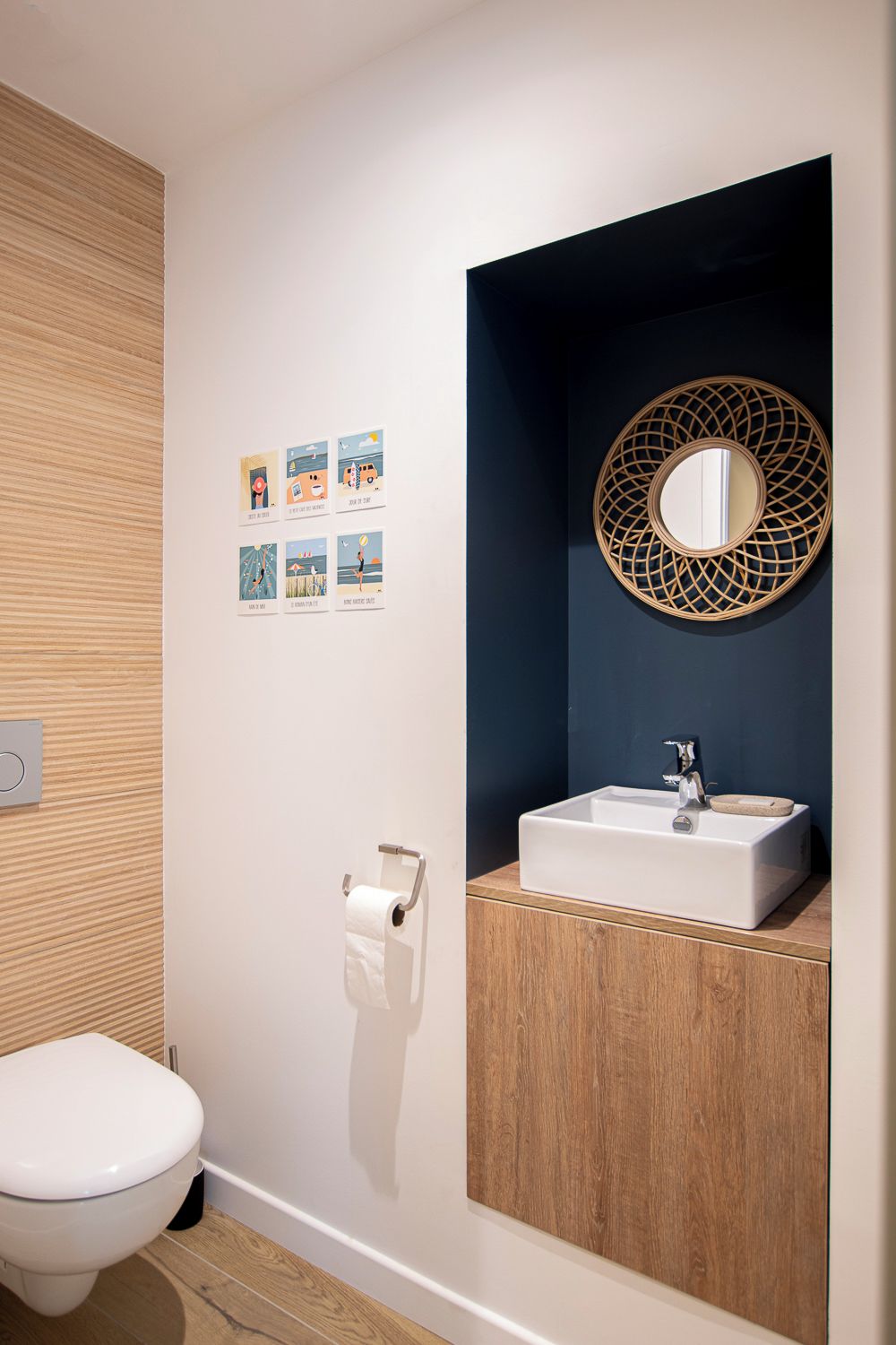 A modern bathroom with a white toilet, a wooden vanity, a white sink, and a wall-mounted mirror with a decorative frame.