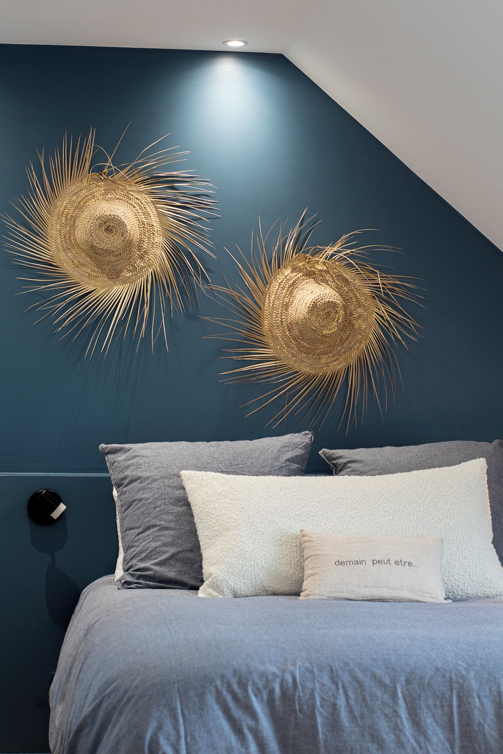 Un dormitorio con pared azul oscuro, una cama con ropa de cama gris y dos elementos decorativos en la pared.