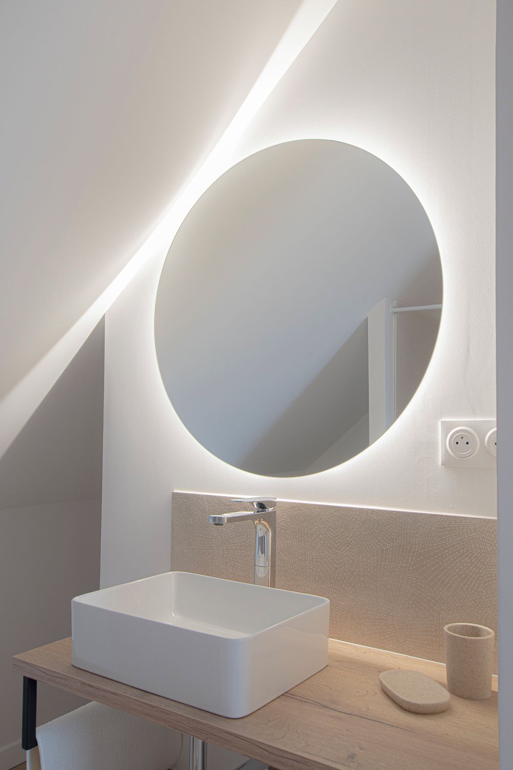 Une salle de bain moderne avec un lavabo blanc, un miroir rond et un luminaire placé au-dessus du miroir.
