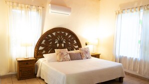 Una cama bien hecha con cabecera de madera, dos mesitas de noche con lámparas y una ventana con cortinas.