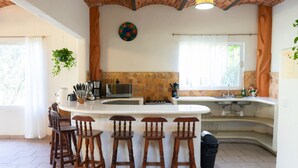 Una cocina con isla central, taburetes de bar, microondas y pileta.