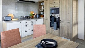 A modern kitchen with white cabinetry, a built-in oven, and a dining area with two chairs. - Bluebell Lodge (South Cerney)
