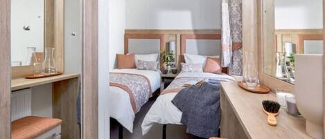 A hotel room with two beds, a desk with a mirror, and a bedside table with a lamp and a hairbrush.