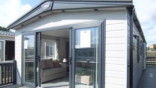 A modern, single-story building with a glass door leading to a furnished balcony. - Bluebell Lodge (South Cerney)