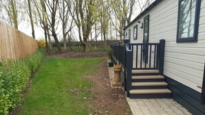 A residential property with a paved pathway leading to a set of steps, a grassy yard, and a wooden fence. - Bluebell Lodge (South Cerney)