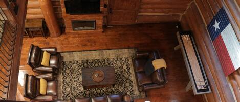 Interior de madera con una escalera, sofás de cuero, una mesa de centro y una bandera de Texas.