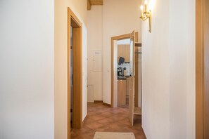 Un couloir avec des portes en bois, une cuisine visible à travers une porte ouverte et un luminaire fixé au mur.