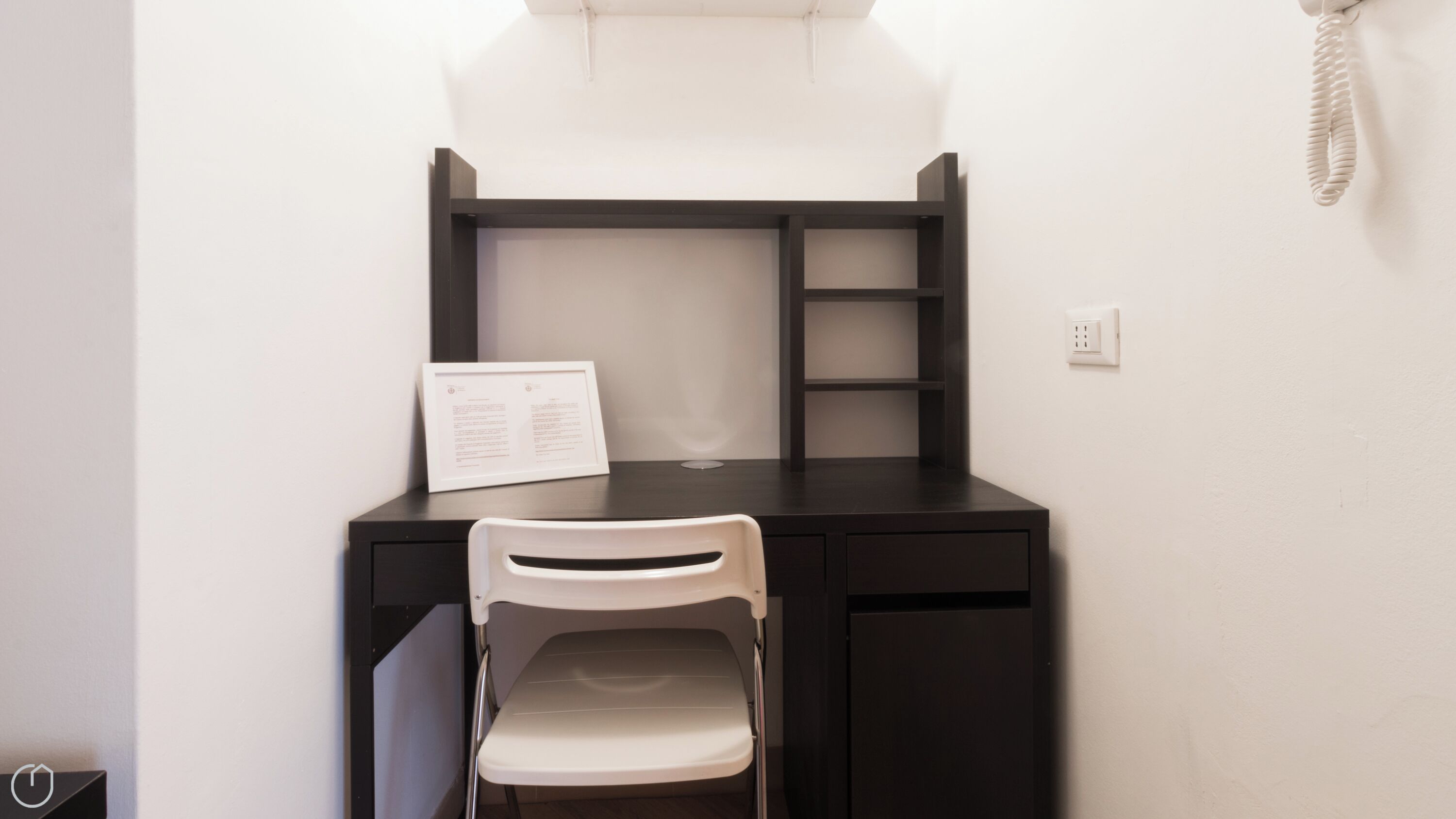 A compact workspace with a desk, chair, and a telephone.