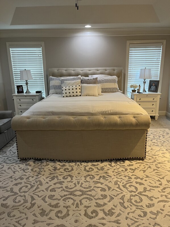 A large bed with a tufted headboard, two bedside tables with lamps, and a patterned carpet.
