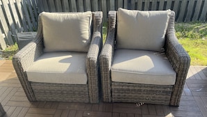 Un sofá de mimbre con cojines, sobre una terraza de madera.