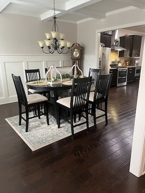 A dining room with a round table, black chairs, a chandelier, and a clock on the wall.