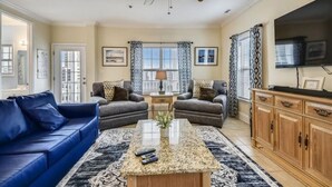 A living room with a blue sofa, two armchairs, a coffee table, and a TV. - Ocean View Luxury Rental - Sleeps 16 (North Myrtle Beach)