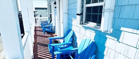 Un porche cubierto con sillas Adirondack azules y una terraza de madera.