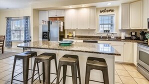 A modern kitchen with white cabinets, a granite countertop, and a built-in island with bar stools. - Ocean View Luxury Rental - Sleeps 16 (North Myrtle Beach)