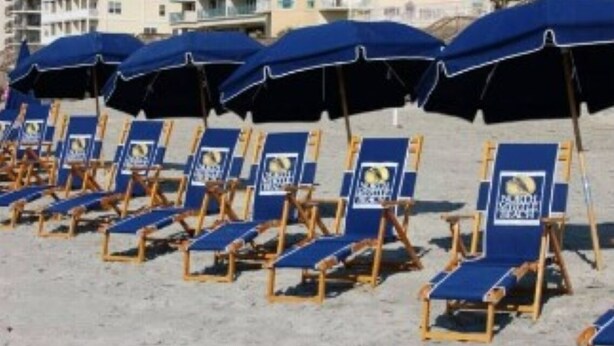 Rows of beach chairs and umbrellas on a sandy beach with buildings in the background. - Ocean View Luxury Rental - Sleeps 16 (North Myrtle Beach)
