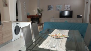 Une cuisine moderne dotée d’un four encastré, d’un lave-linge et d’un coin repas avec une table en verre et un canapé bleu.