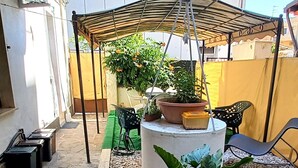 Un espace extérieur abrité, doté d’un sol en béton, de plantes en pot, d’une table et d’une chaise.
