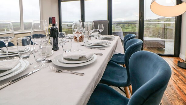 A dining area with a table set for four, large windows, and a view of the countryside. - Glenhurst (Dronfield)