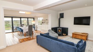 A modern living room with a sofa, a dining area with a table set for four, a fireplace, and a TV mounted on the wall. - Glenhurst (Dronfield)