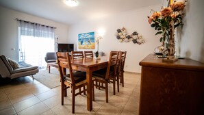 Ein Essbereich mit Holztisch und Stühlen, einer Couch und einem Fernseher im Hintergrund.