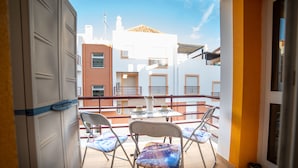 Ein Balkon mit zwei Stühlen und einem Tisch, mit Blick auf ein Gebäude mit zahlreichen Fenstern und einem Ziegeldach.