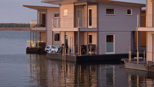 A multi-story houseboat with balconies, a deck area, and a dock. - Boat 'Floating House' with Lake View, Private Terrace and Wi-Fi (Kröslin)