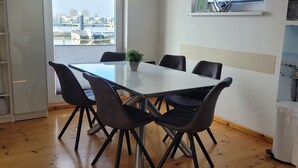 A room with a wooden floor, a white table with four chairs, a potted plant, and a window with a view of buildings. - Boat 'Floating House' with Lake View, Private Terrace and Wi-Fi (Kröslin)