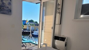 A hotel room with a bed, a window, a door, and a view of boats and a flag. - Boat 'Floating House' with Lake View, Private Terrace and Wi-Fi (Kröslin)