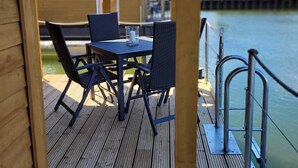 A wooden deck with a table and chairs, overlooking a body of water. - Boat 'Floating House' with Lake View, Private Terrace and Wi-Fi (Kröslin)