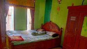 A single bed with a wooden headboard in a room with green walls and a wooden wardrobe. - Indo Hometown (Garut)
