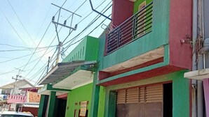 A multi-story building with a green facade, a red balcony, and a closed shuttered door. - Indo Hometown (Garut)