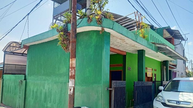 A green building with a gated entrance, a parked car, and a visible utility pole. - Indo Hometown (Garut)