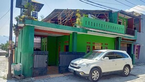 A two-story building with a green facade, a white car parked in front, and a sign indicating a business or service. - Indo Hometown (Garut)