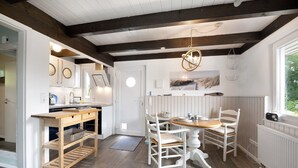 A kitchen with white cabinetry, a wooden table, and chairs, a hanging light fixture, and a window with a view of greenery.