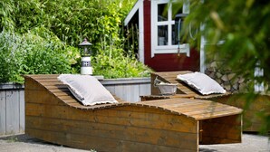 A wooden deck with two benches, a lantern, and a red building in the background.