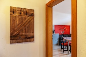 Un porte-manteau mural en bois, un coin repas avec une table et des chaises, et un espace cuisine avec un mur rouge et des décorations suspendues.