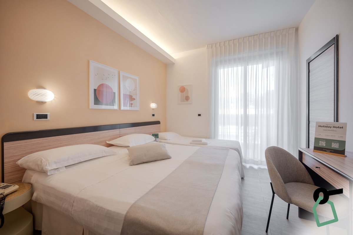 Quarto de hotel com duas camas, uma escrivaninha, uma cadeira e obras de arte nas paredes.