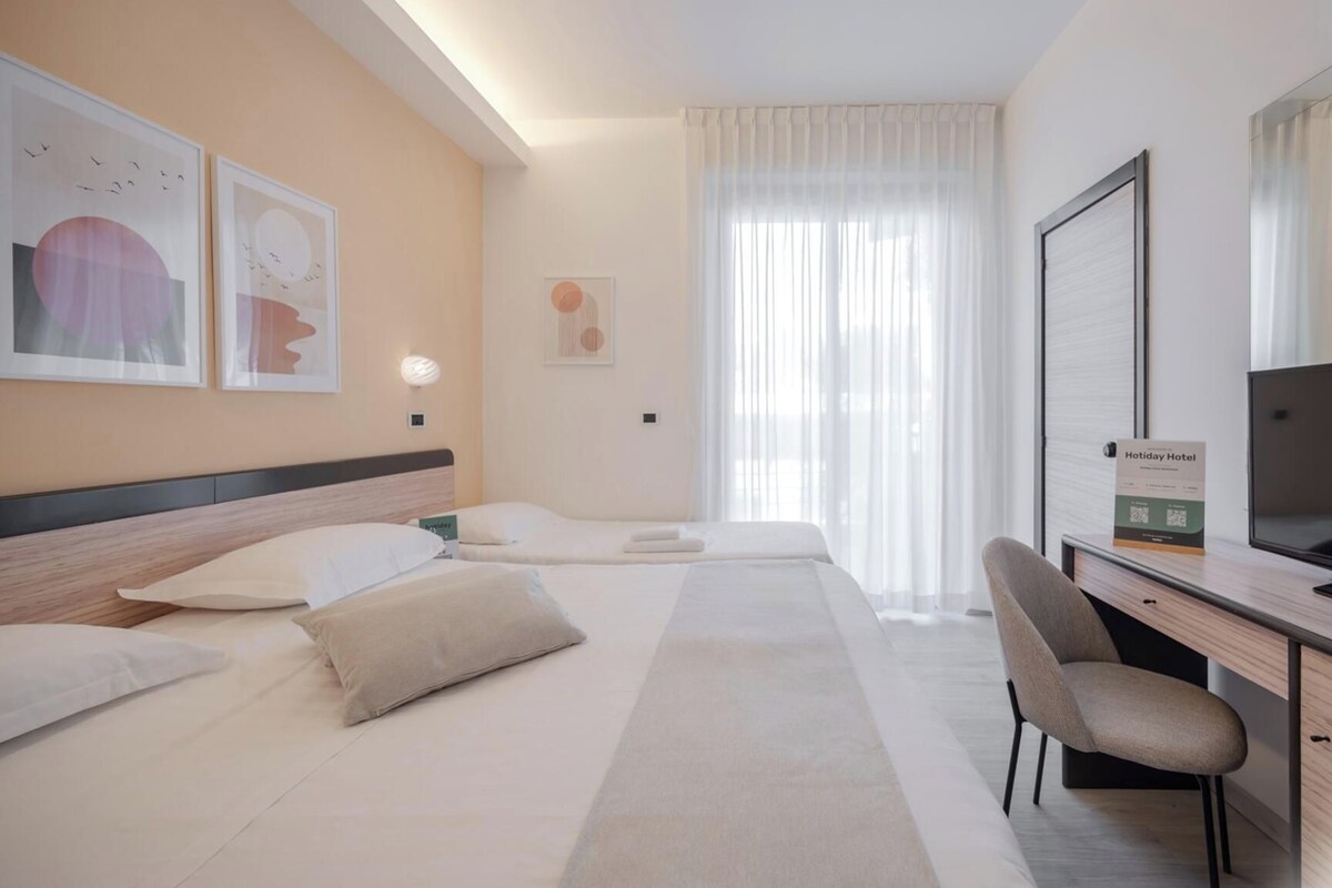 A hotel room with a bed, a desk, a chair, and a TV.