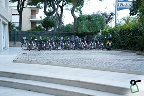 Une rangée de vélos est stationnée sur une zone pavée, avec des marches menant à un bâtiment.