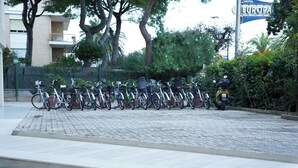 Una fila de bicicletas estacionadas en un área pavimentada, con un edificio y árboles de fondo.