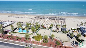 Un complexe hôtelier de bord de mer avec des rangées de parasols, une piscine et des palmiers.