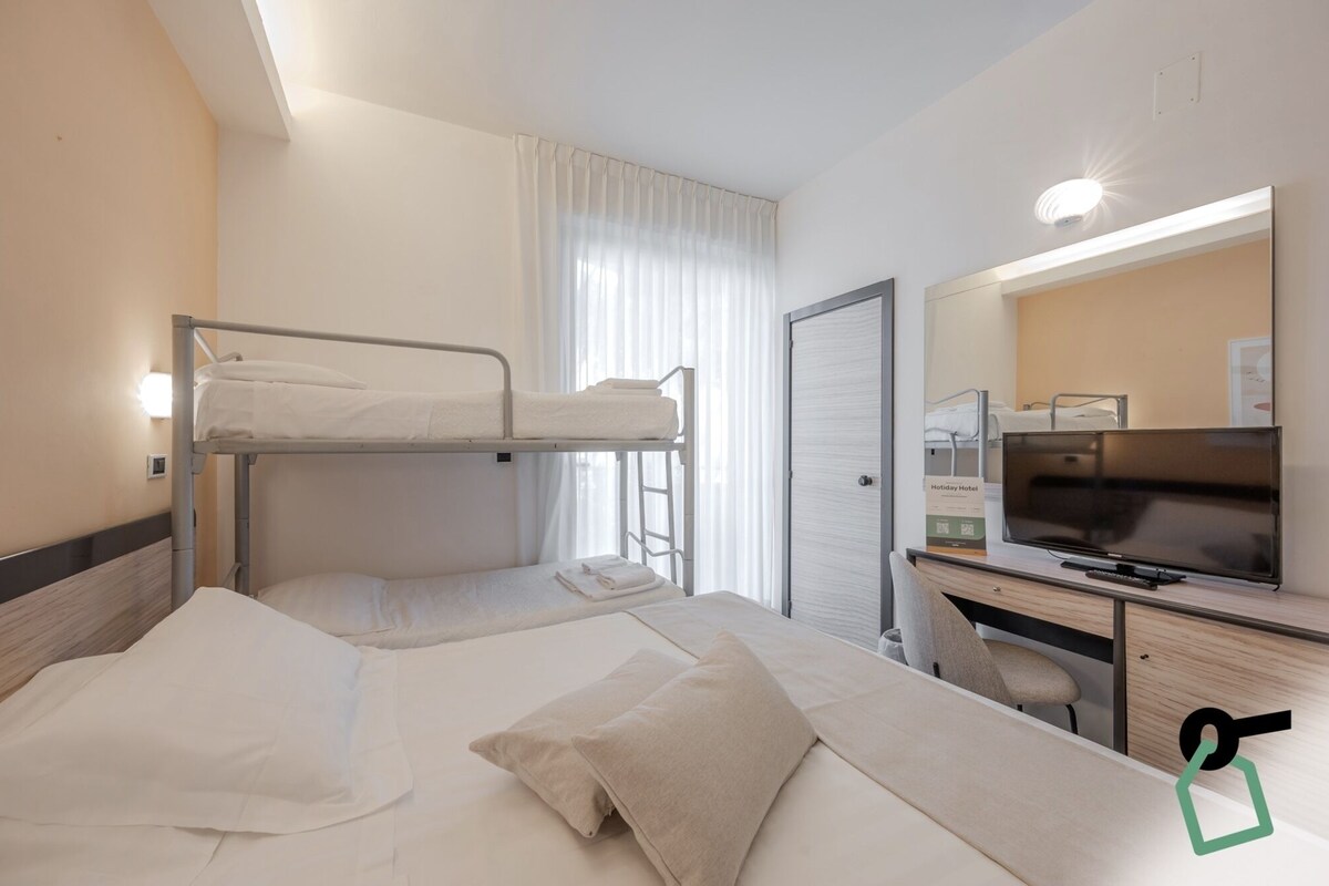 Une chambre d’hôtel avec deux lits superposés, un bureau avec une télévision et un miroir.